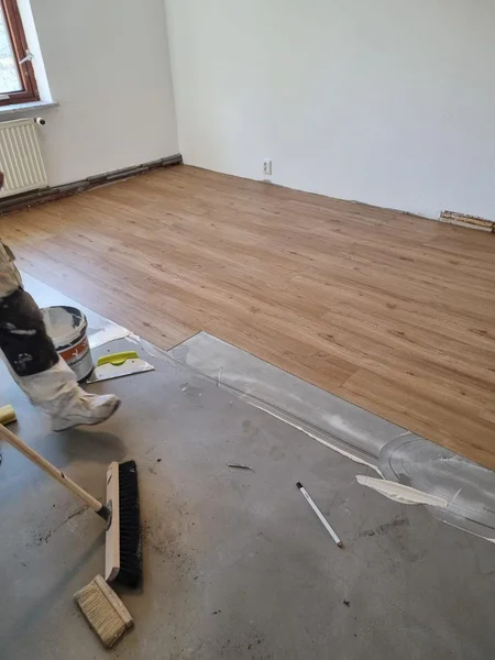 Handwerker verlegt neuen Designbelag auf frisch vorbereitetem Estrich in Kappeln