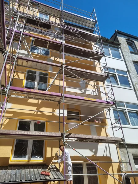 Ein Handwerker auf dem Gerüst reinigt ein kleines Dach unterhalb der gelb gestrichenen Fassade