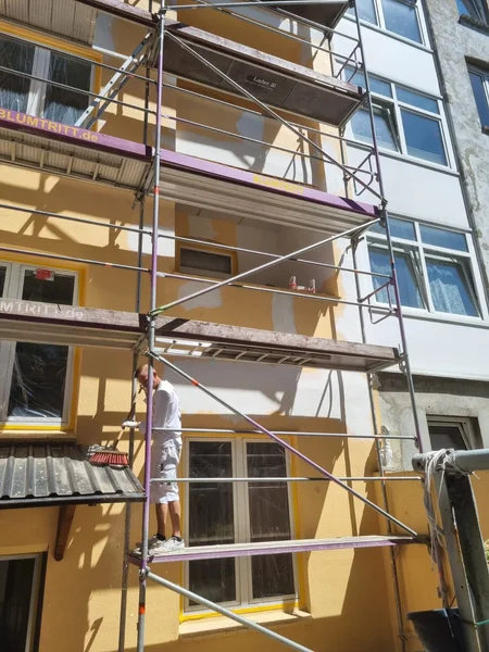 Ein Handwerker steht auf dem Gerüst und arbeitet an der gelben Fassade des Wohnhauses