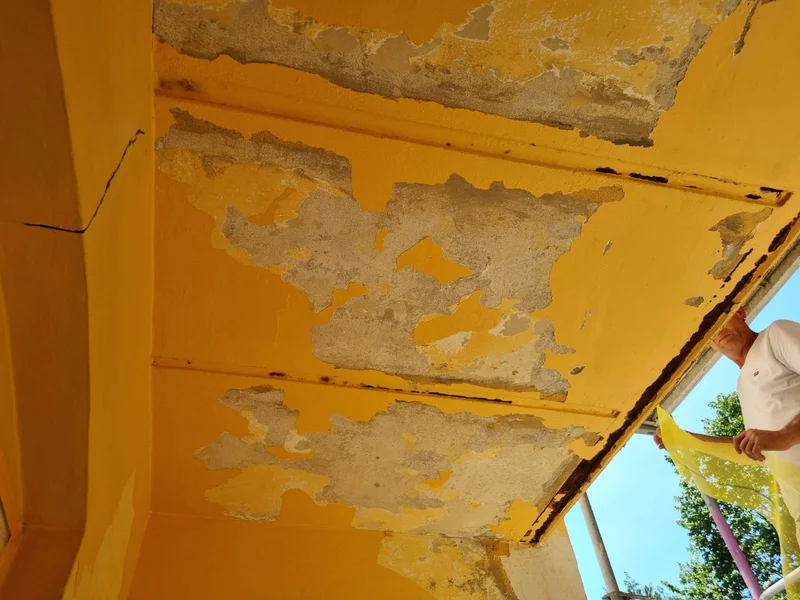 Nahaufnahme einer Balkondecke mit großflächig abblätternder Farbe und rostigen Streben