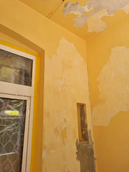 Balkonecke mit stark abgeplatztem gelbem Putz neben einem Fenster und einer kleinen Wandnische