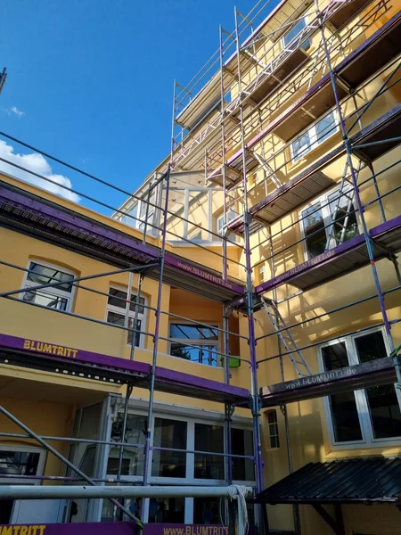 Gesamtansicht des Gerüstaufbaus im Innenhof an der hohen gelben Fassade mit vielen Fenstern und Balkonen