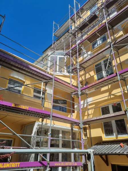 Lila-graues Arbeitsgerüst an der Rückseite eines mehrstöckigen gelben Wohnhauses vor blauem Himmel
