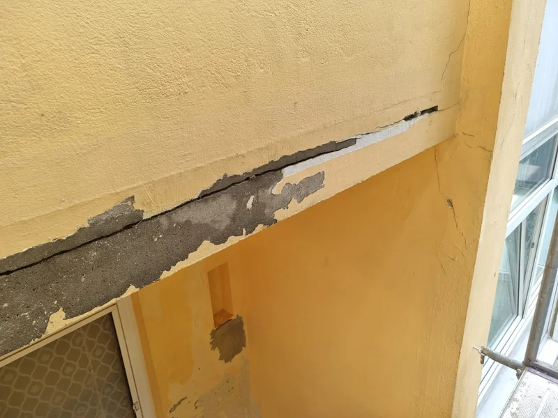 Offener Riss und abgeplatzter Putz an der Fassade vor der Sanierung, darunter ein Fenster mit Gitter
