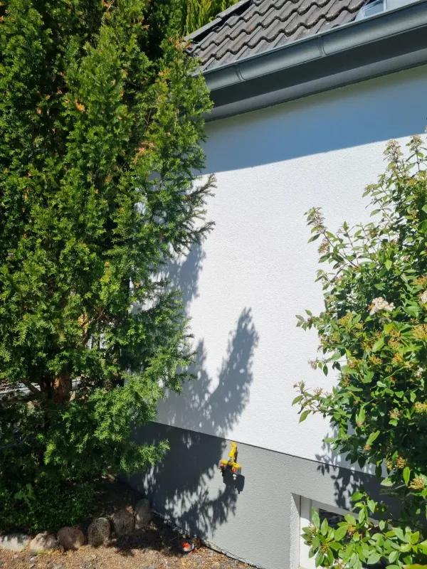Hausecke mit frisch gestrichener Fassade, umgeben von Bäumen und Sträuchern