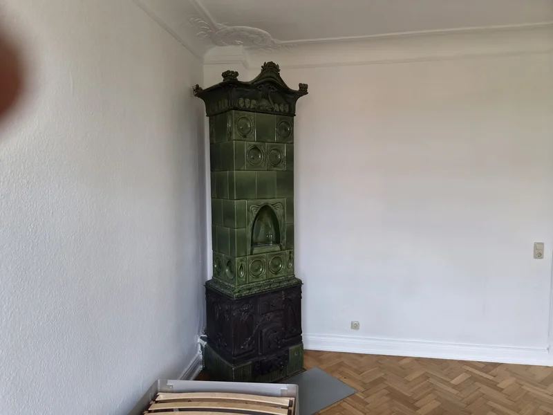Frisch gestrichene Wände und Stuckdecke rund um den historischen grünen Kachelofen