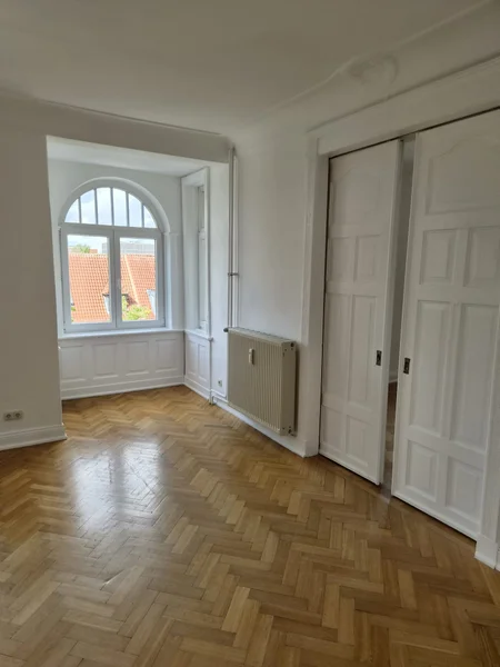 Zimmer mit Rundbogenfenster, frisch gestrichenen Wänden und lackierten Schiebetüren des Einbauschranks