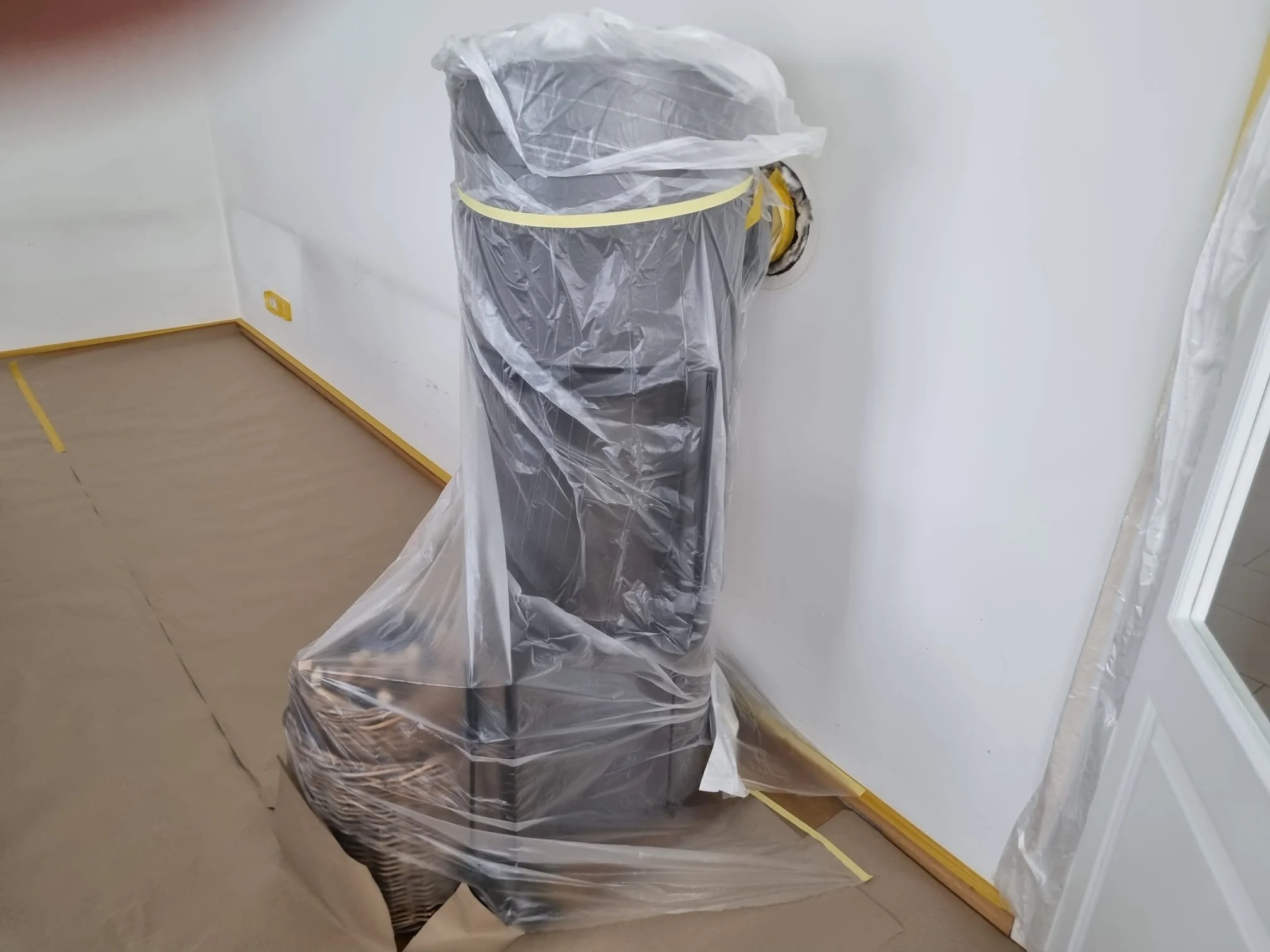 Ein Heizkörper komplett mit Folie eingepackt und mit gelbem Klebeband abgeklebt, der Boden ist mit Malervlies geschützt