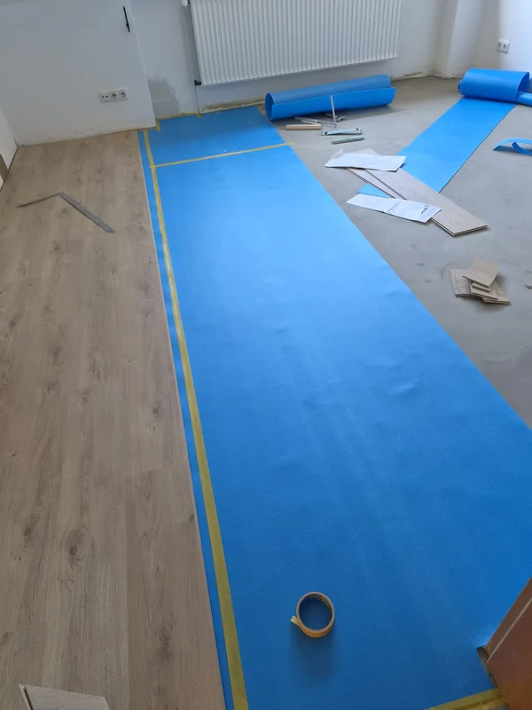 Die blaue Trittschalldämmung wird ausgerollt, während nebenan schon die ersten Laminatdielen liegen